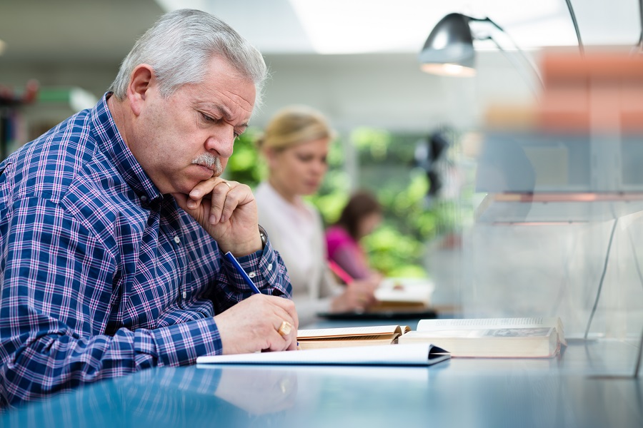 Senior man studying among young people in library